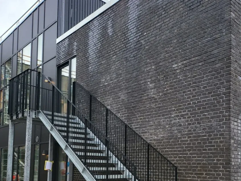 Nyere erhvervsbyggeri med mørk murstensfacade og udvendig trappe